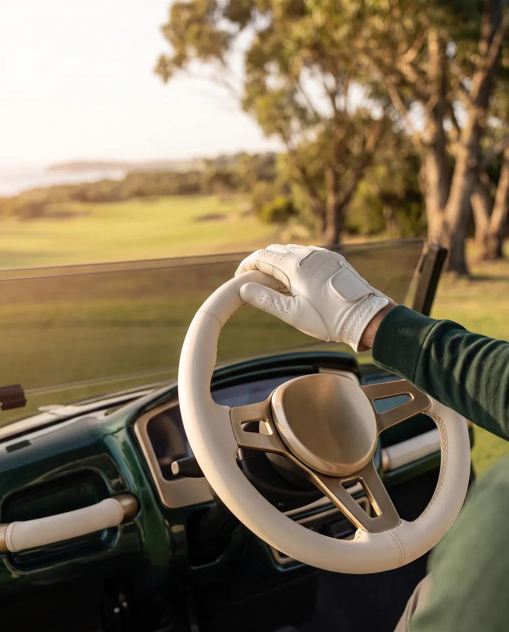 Gloved hand on the ivory leather steering wheel of a luxury golf cart